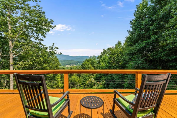 Wooden deck with two rocking chairs overlooking forested mountains and valley under clear blue sky